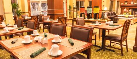 Un hall de hotel con varias mesas de comedor dispuestas con vajilla blanca, una chimenea y una zona de estar con sofás y sillones.