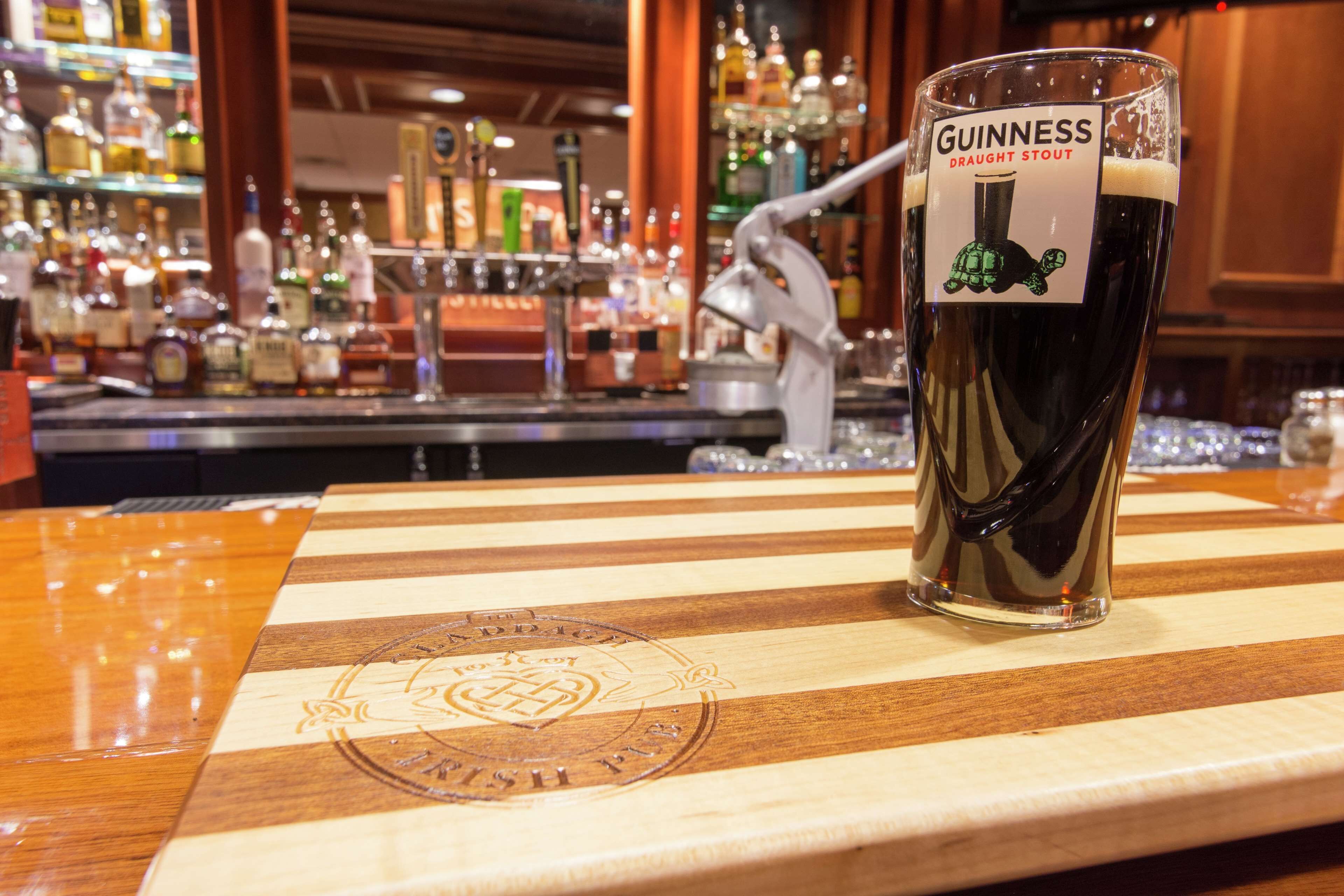 A glass of Guinness on a wooden bar counter with a bar in the background.