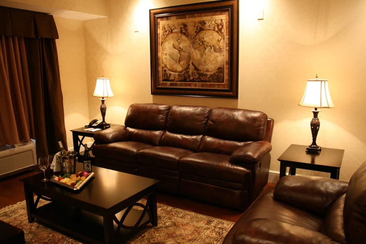 A living room with a brown leather sofa, a coffee table with a tray of food and drinks, two side tables with lamps, and a large framed map on the wall.