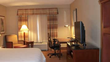 A hotel room with a bed, a desk with a chair, a television, and a lamp.