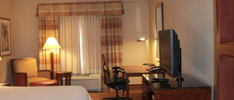 A hotel room with a bed, a desk with a chair, a television, and a lamp.