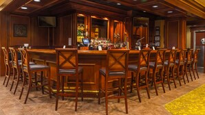 A bar area with wooden bar counters and chairs, a television mounted on the wall, and a variety of bottles and glasses on the shelves. - Hilton Garden Inn Bangor (Bangor)