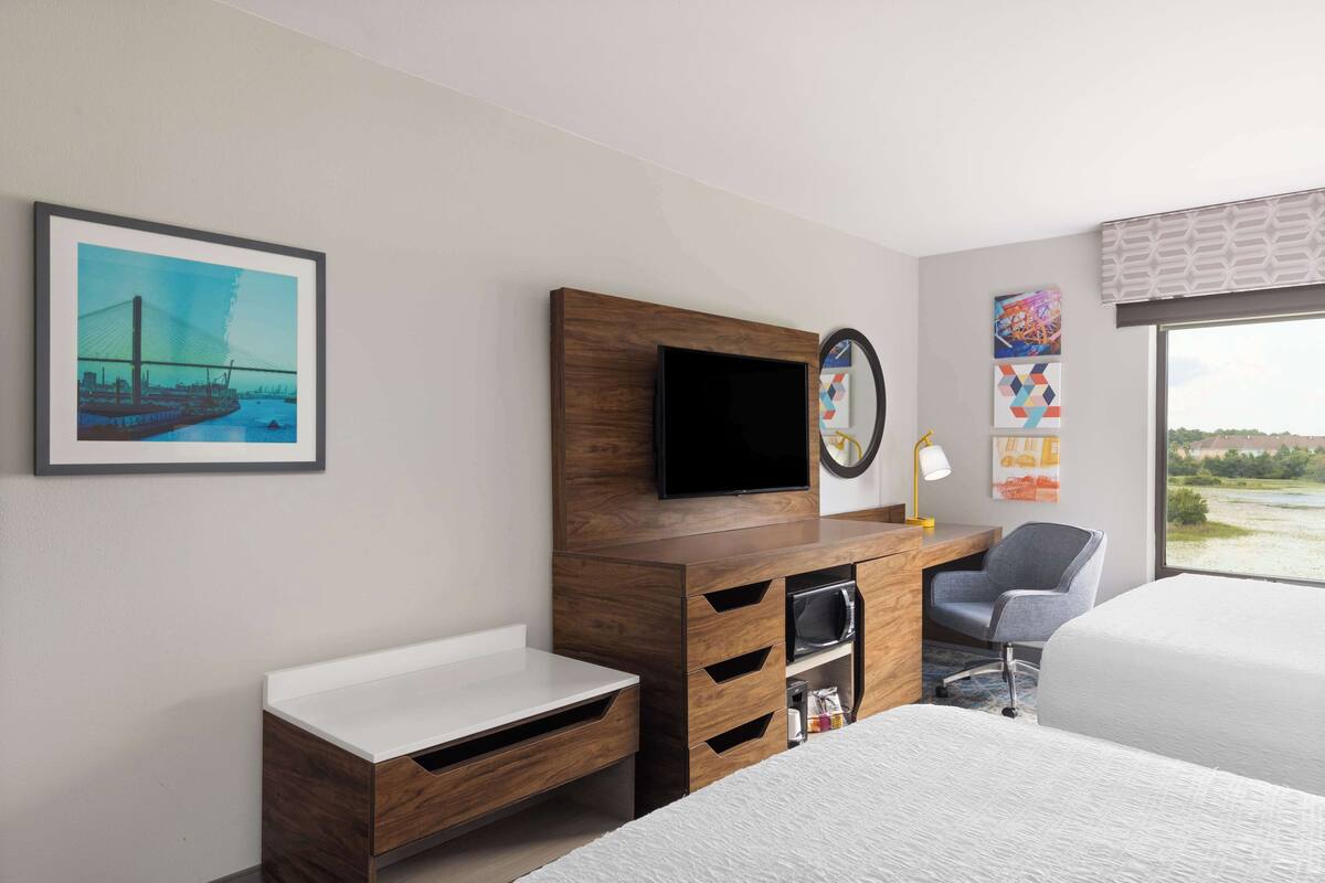 A hotel room with a bed, a desk with a flat-screen TV, a chair, and a window with a view of the outdoors.