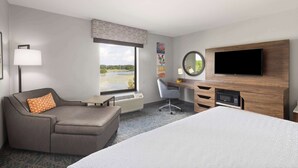 A hotel room with a bed, a desk, a chair, a TV, and a window with a view of a body of water.