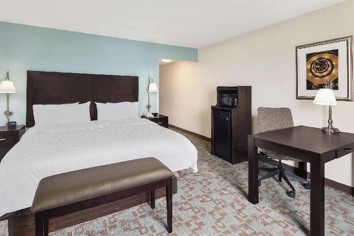 A hotel room with a bed, a desk, a chair, a television, and a lamp.