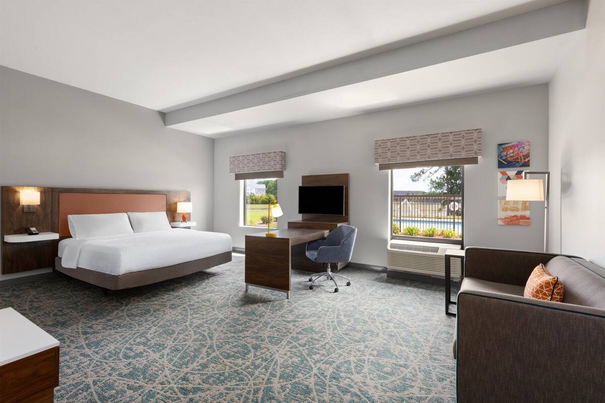 A hotel room with a bed, desk, chair, and a sofa.
