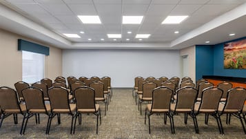 A conference room with rows of chairs, a carpeted floor, and a projector screen.