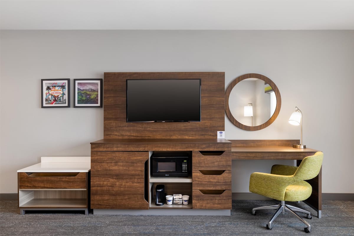 A hotel room with a wooden desk, a flat-screen TV, a microwave, a coffee maker, and a yellow chair.