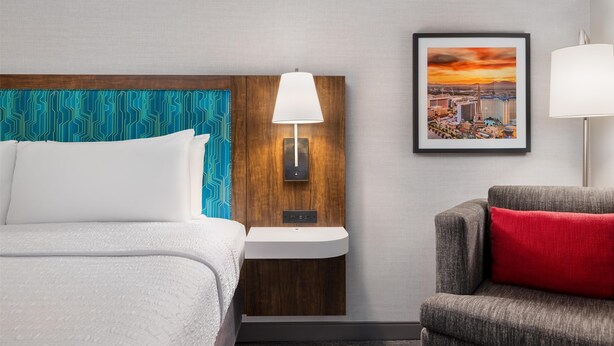 Une chambre d’hôtel avec un lit, une table de chevet avec une lampe, une chaise et un tableau encadré au mur.