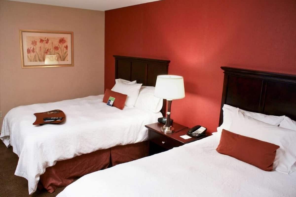 Une chambre d’hôtel avec deux lits, une table de chevet avec une lampe et un téléphone, et un tableau encadré au mur.