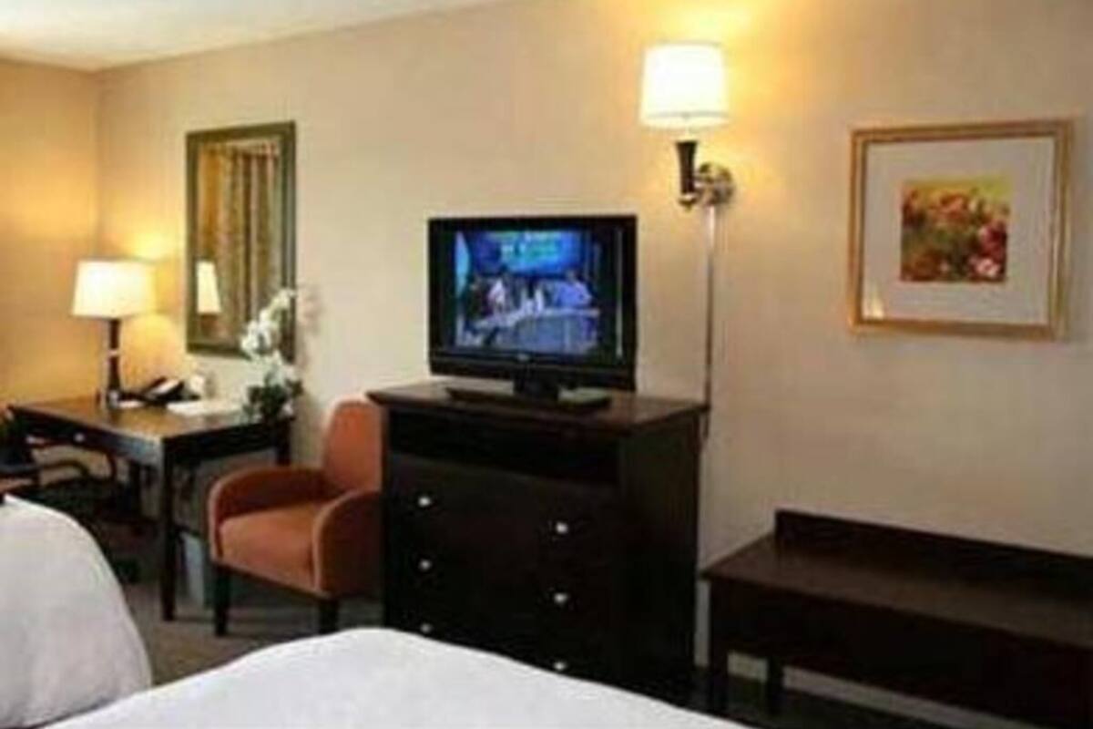 A hotel room with a bed, a desk with a lamp, a television, a chair, and a dresser.