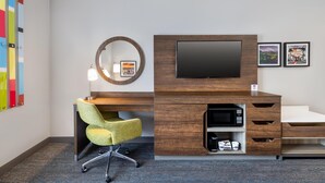 Une chambre d’hôtel moderne avec un bureau en bois, un téléviseur à écran plat, un miroir rond et une chaise.