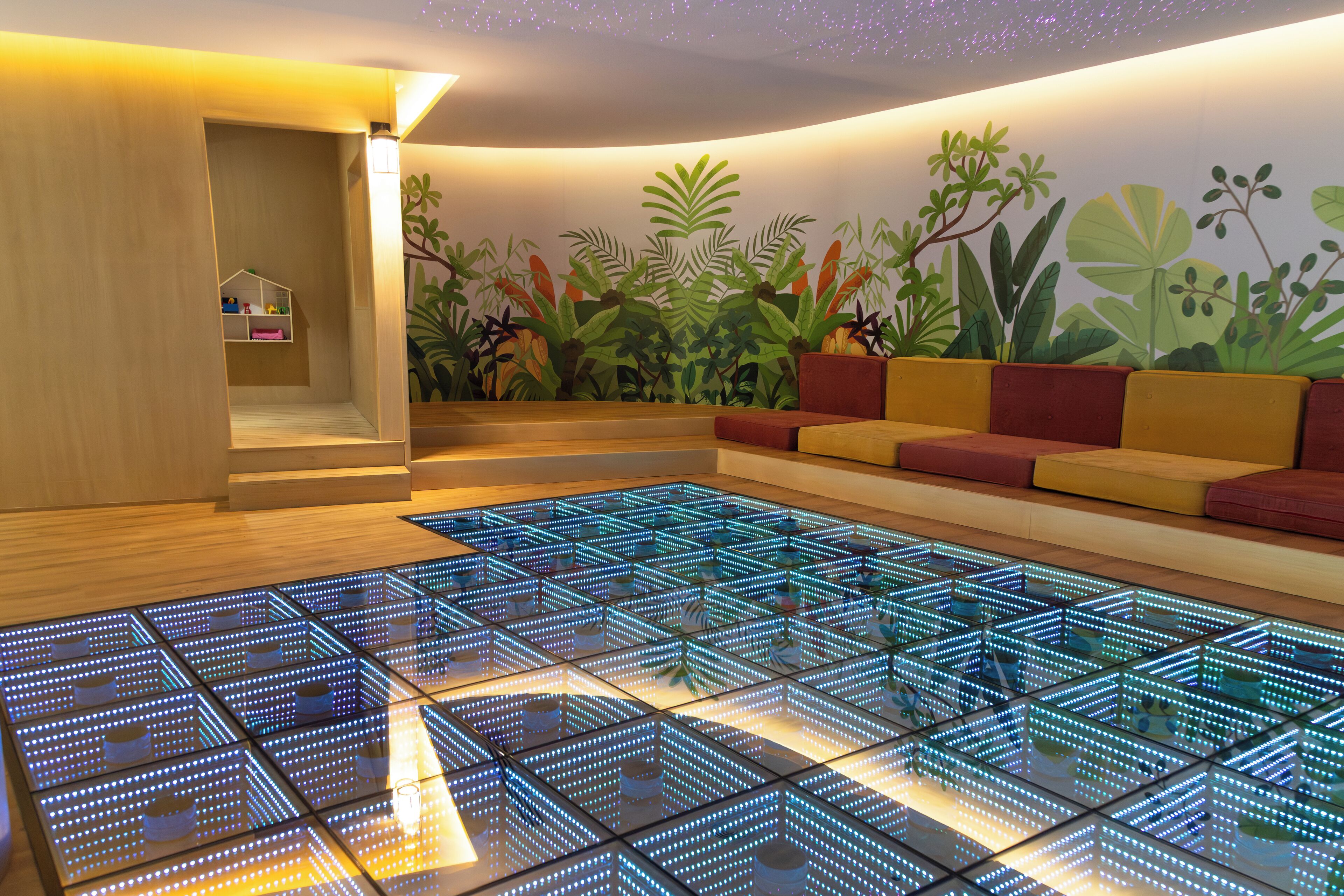 A modern room with a geometric light floor, a seating area with cushions, and a wall mural of tropical plants.