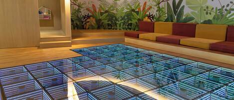 Una habitación moderna con suelo de diseño geométrico, una zona de estar con cojines y un mural de plantas tropicales.