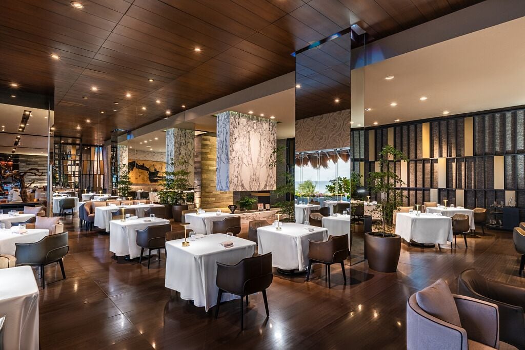 A spacious restaurant with multiple tables and chairs, a high ceiling with recessed lighting, and a view of the outdoors.