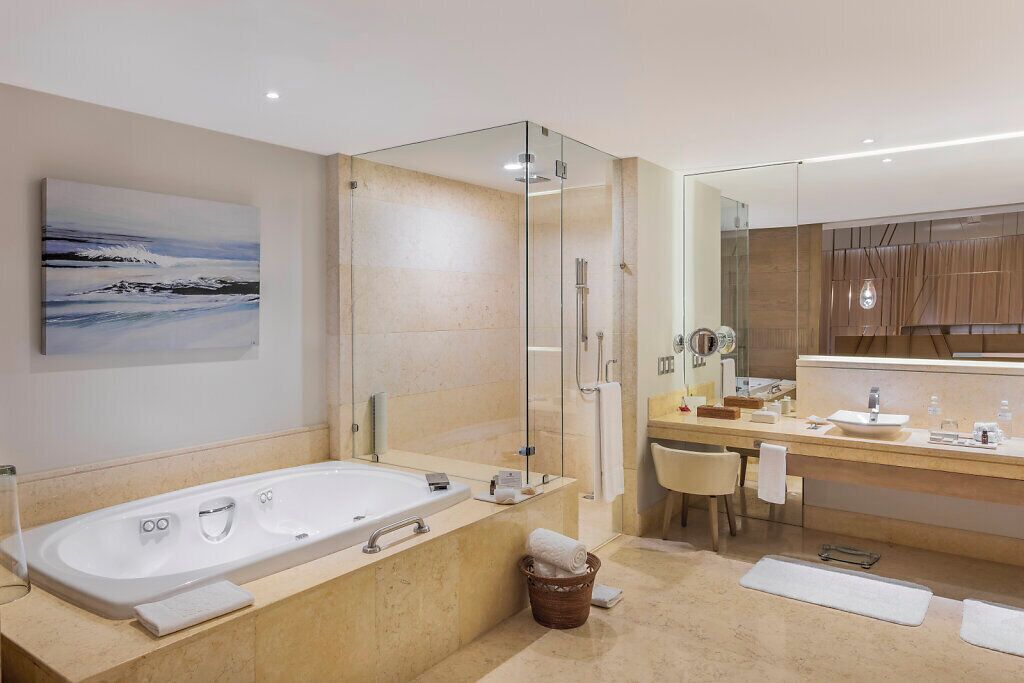 Une salle de bain moderne avec une grande baignoire, une douche à l’italienne, un meuble-lavabo avec un miroir et un tableau au mur.