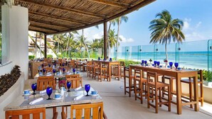 Ein Restaurant direkt am Strand mit Außenbereich, Palmen und Meerblick.