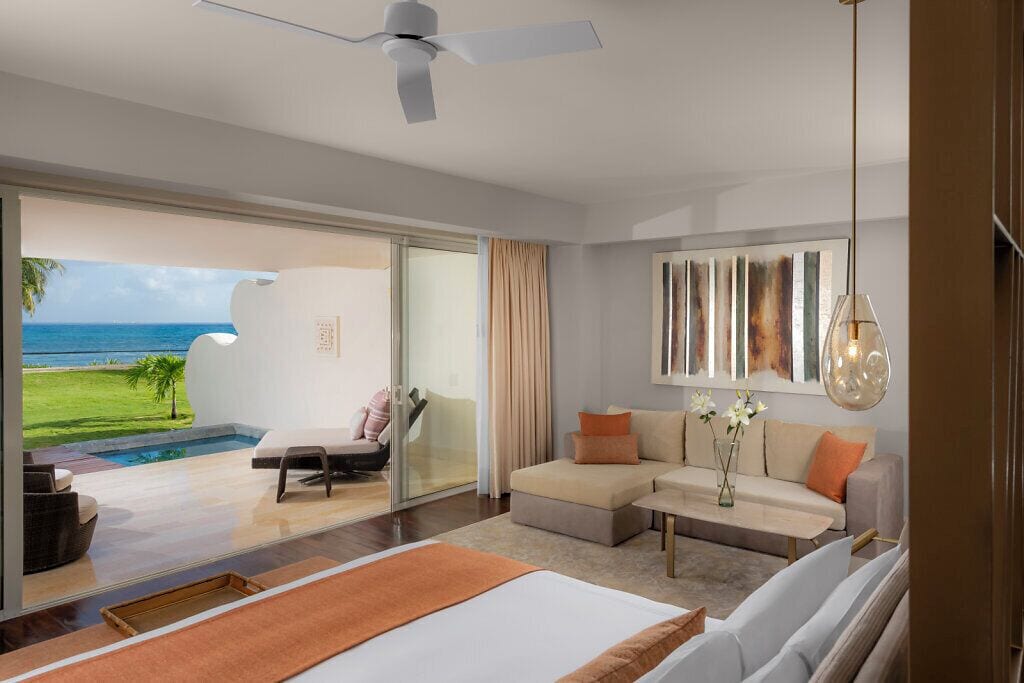 A modern hotel room with a large bed, a sofa, a coffee table, and a view of the ocean.