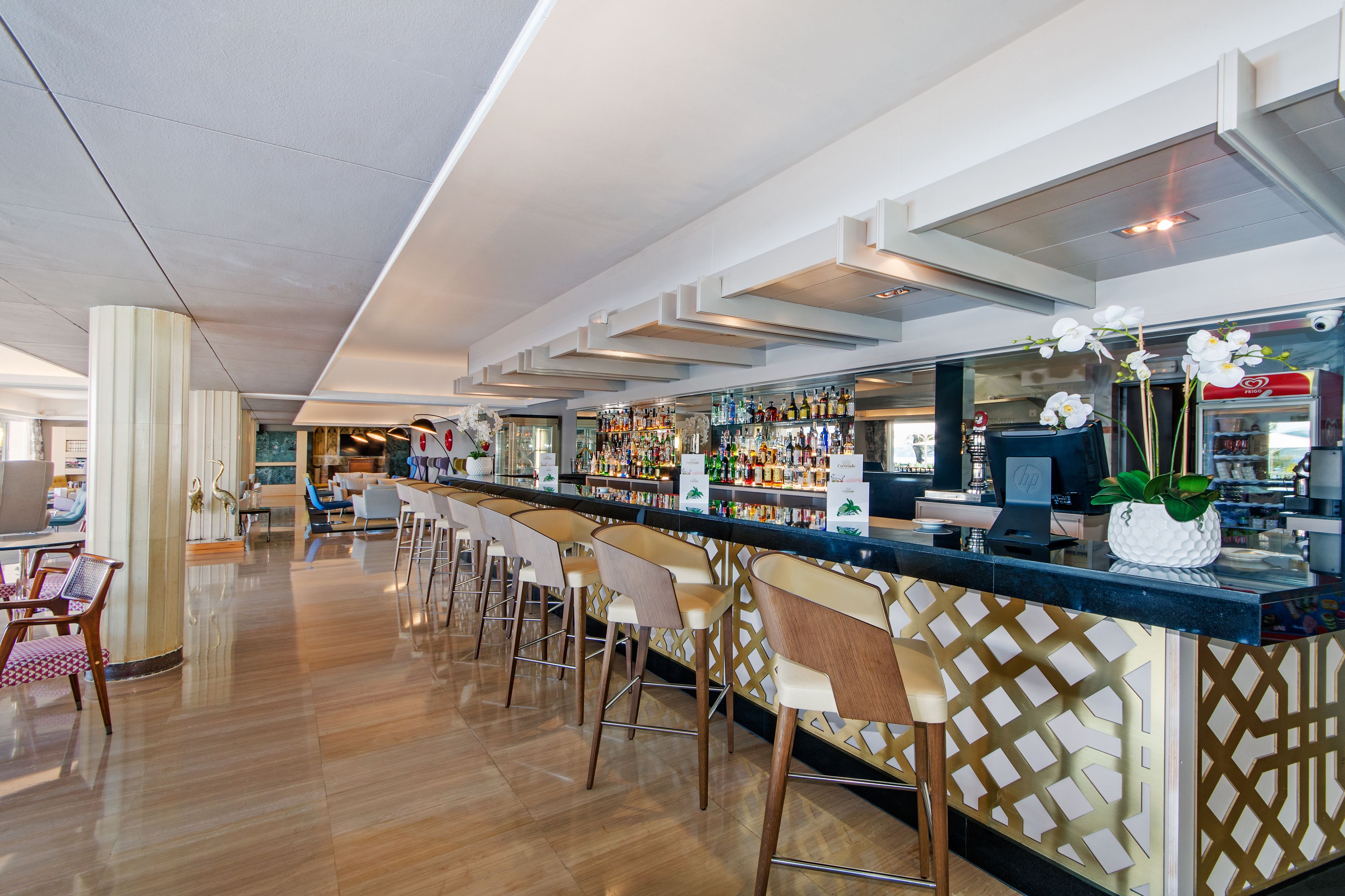 Eine Bar mit einer langen Theke, mehreren Barhocker und einer Auswahl an Flaschen und Gläsern.