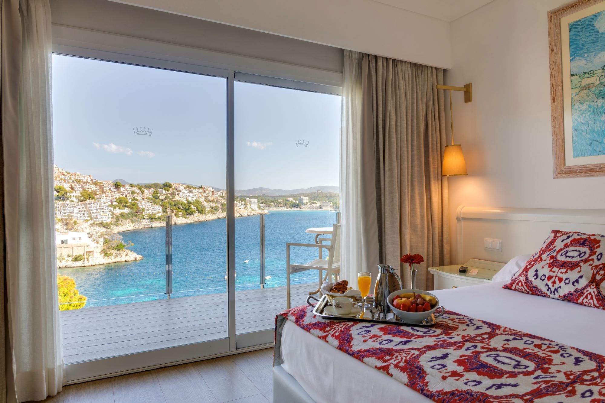 A hotel room with a balcony overlooking a coastal town and the sea.