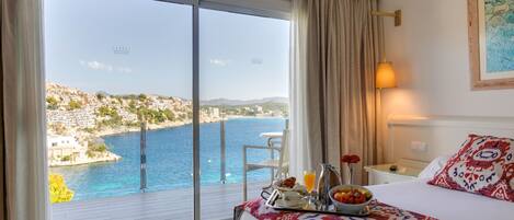 A hotel room with a balcony overlooking a coastal town and the sea.