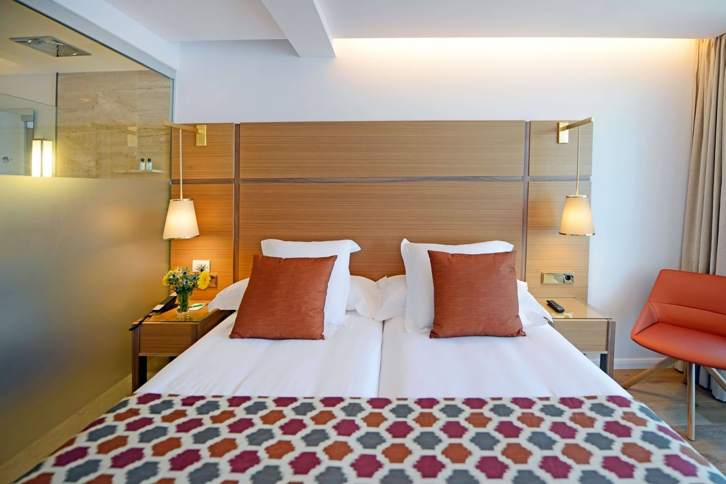 A hotel room with a large bed, two bedside tables, a nightstand, a chair, and a mirror.