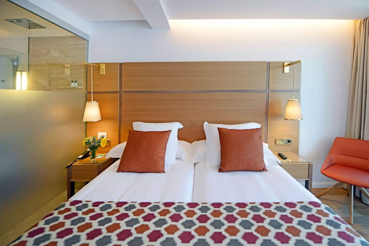 A hotel room with a large bed, two bedside tables, a nightstand, a chair, and a mirror.