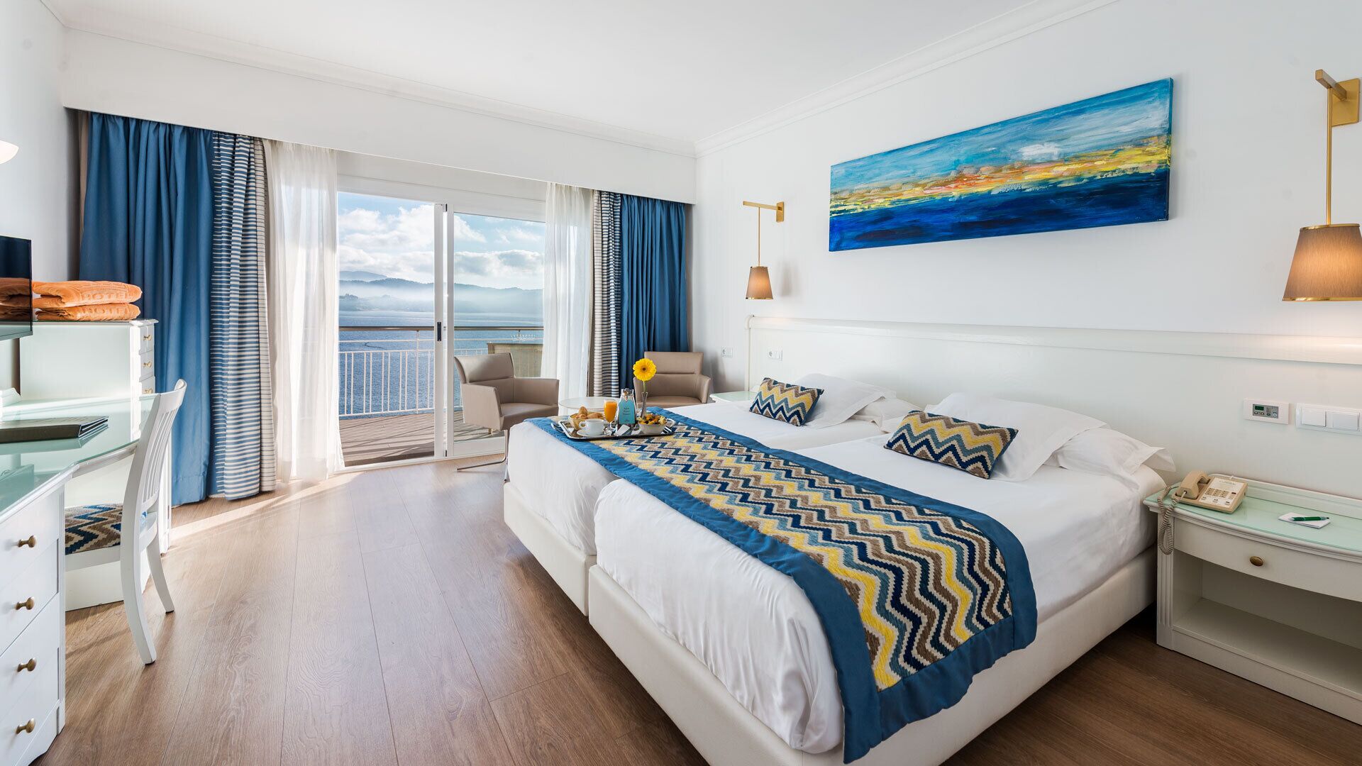 A hotel room with a large bed, a desk, a chair, and a view of the sea.