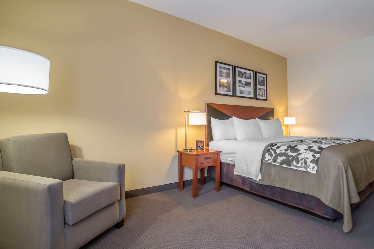 A hotel room with a bed, a chair, a nightstand, and two wall-mounted lamps.