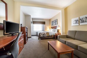 Quarto de hotel com cama, escrivaninha com televisão, sofá e mesa de centro.