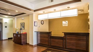 Zona de recepción de hotel con mostrador, un reloj y felpudo de bienvenida.
