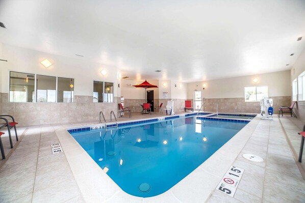 Piscina interior com faixas de separação bem definidas, um guarda-sol vermelho e uma área de estar com cadeiras.