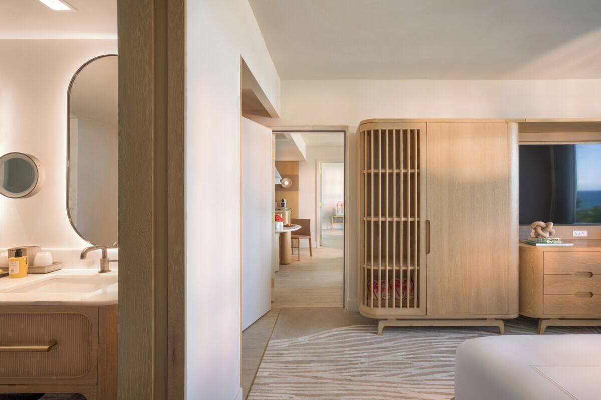 A modern bedroom with a large bed, a wardrobe, a vanity with a mirror, and a view of the outdoors.