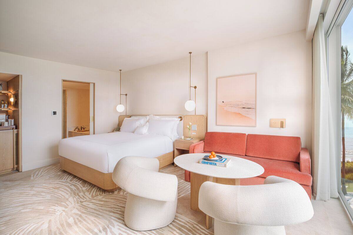 A modern hotel room with a large bed, a sofa, a round coffee table, and a view of the ocean.