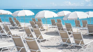 A beach with rows of white sun loungers and white umbrellas, arranged in a neat pattern.