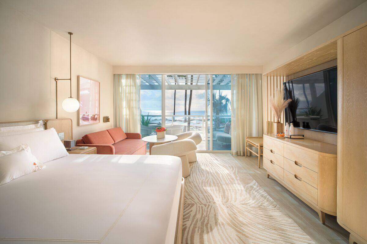 A hotel room with a large bed, a TV, a desk, a chair, a sofa, and a view of the ocean.