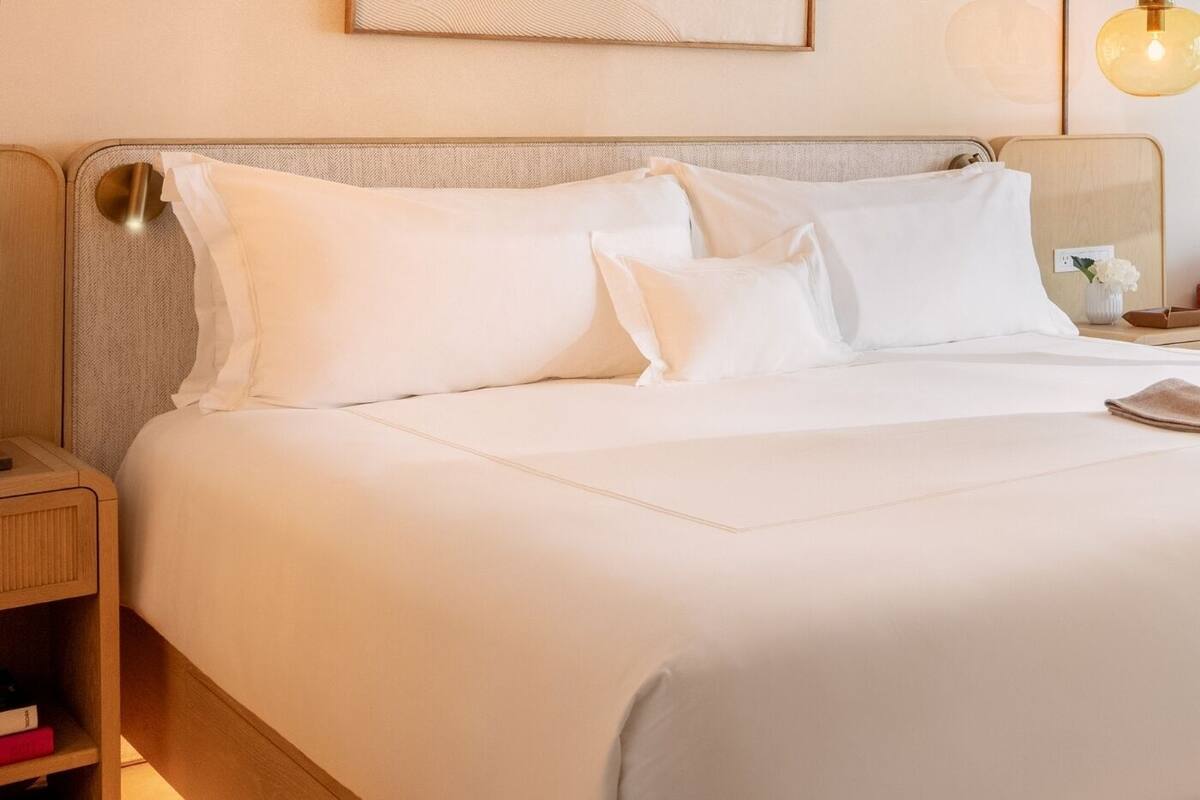 A neatly made bed with white linens and a wooden headboard.