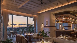 A restaurant with a bar, seating areas, and large windows overlooking a scenic view.