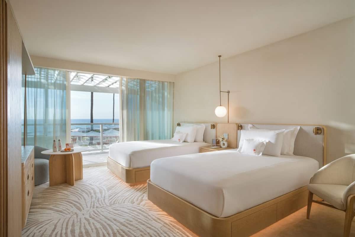 A hotel room with two beds, a sitting area, a balcony with a view, and a large window.