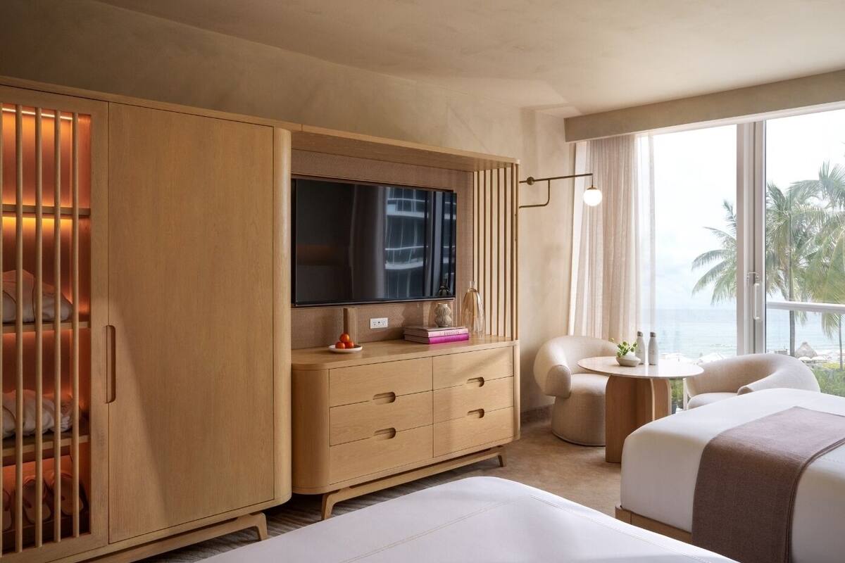 A hotel room with a large wooden wardrobe, a flat-screen TV, a small round table, a sofa, and a bed.