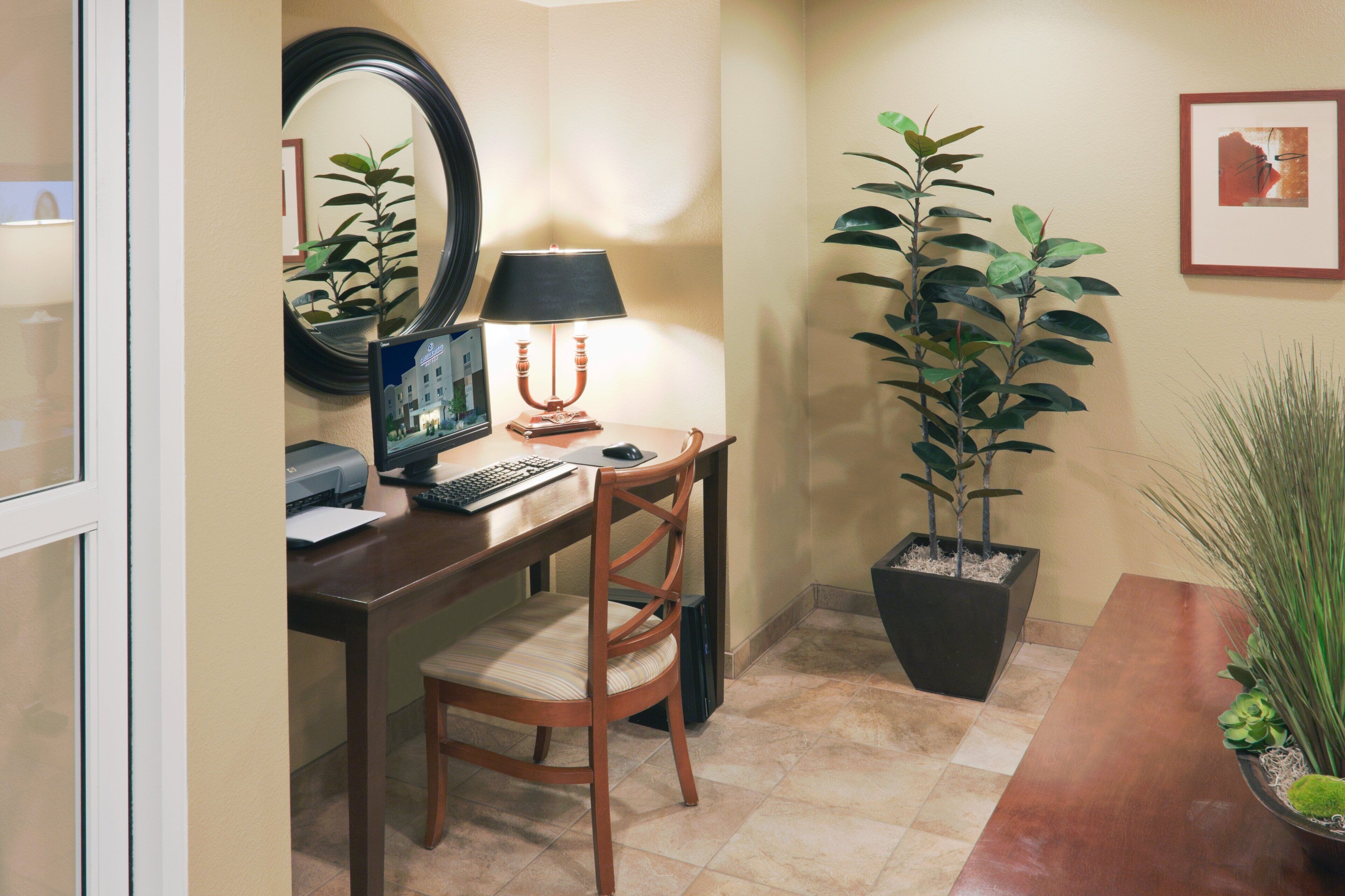 A home office with a desk, computer, lamp, chair, and potted plants.
