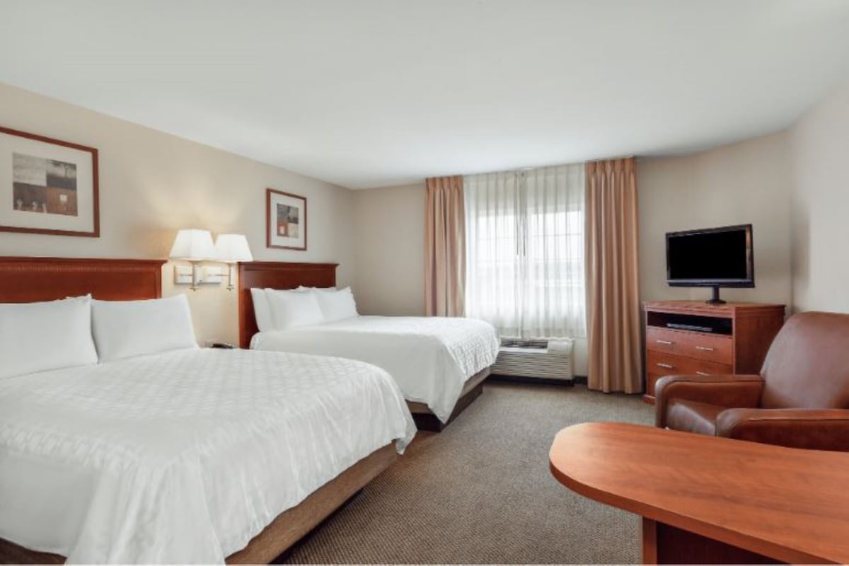 A hotel room with two beds, a desk, a chair, a television, and a window with curtains.