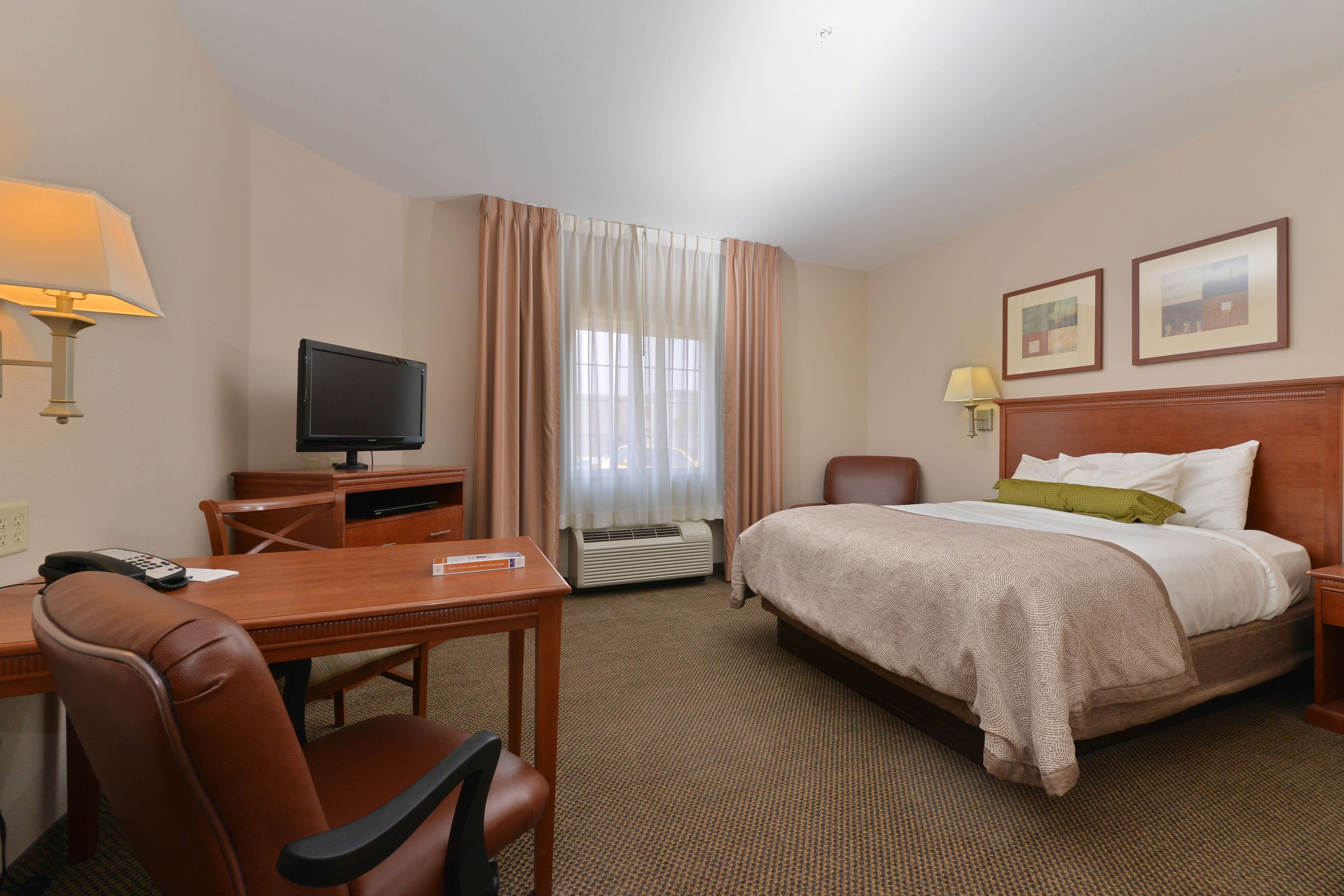 A hotel room with a bed, desk, chair, television, and a window with curtains.