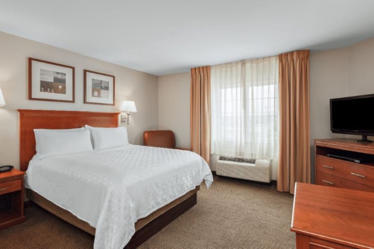 A hotel room with a bed, a desk, a television, and a window with curtains.