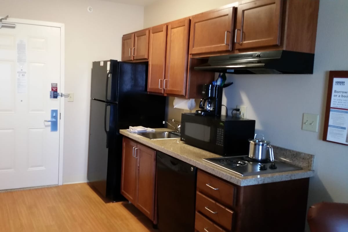 A compact kitchen with wooden cabinets, a black refrigerator, a microwave, and a stainless steel sink.
