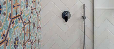 A shower area with a herringbone-patterned tiled wall, a showerhead, and a handheld shower attachment.