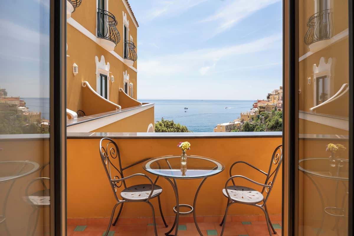 Un balcon avec une table en verre et deux chaises, offrant une vue sur le paysage urbain de la côte.