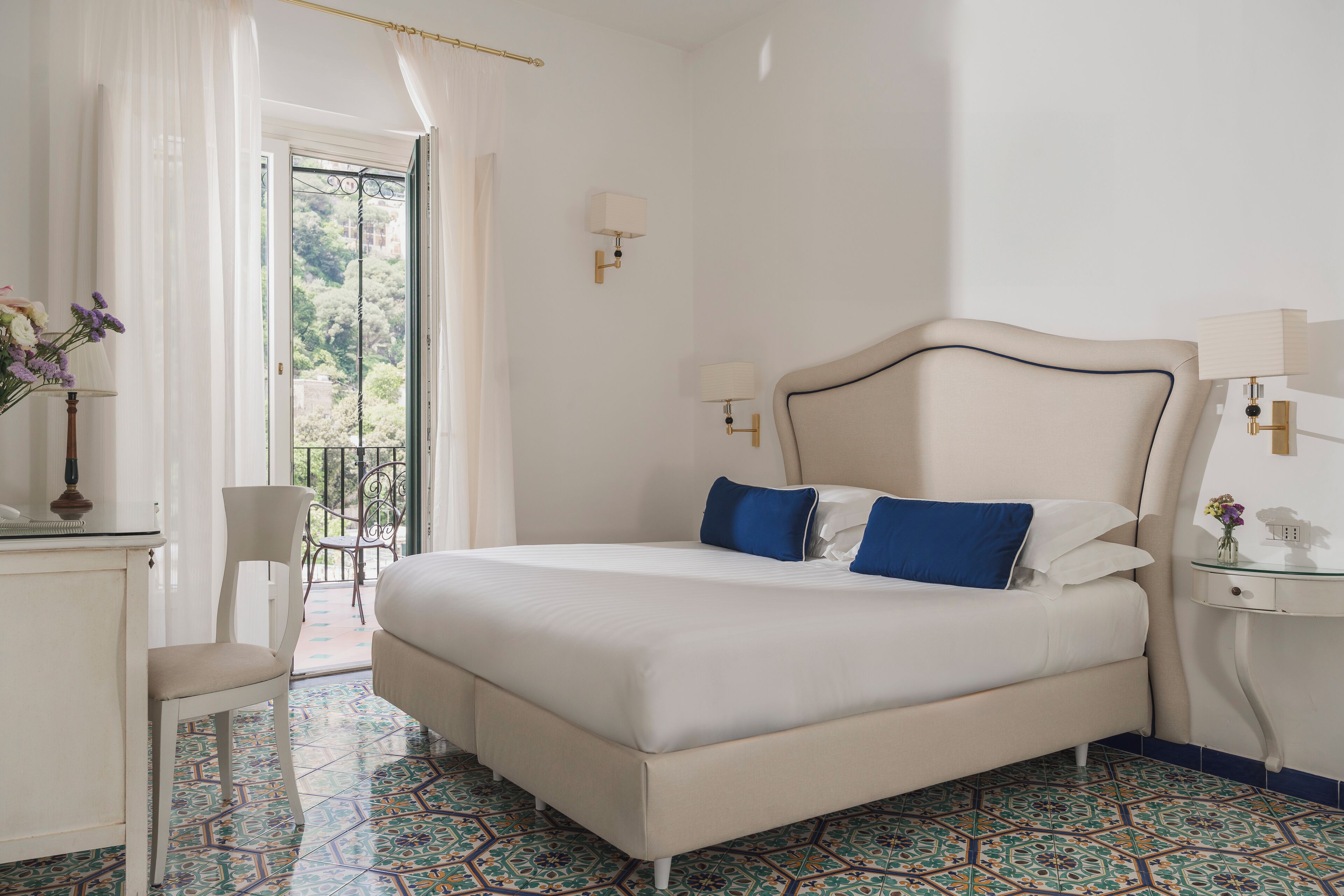 Quarto com cama, cadeira, escrivaninha e varanda com vista.