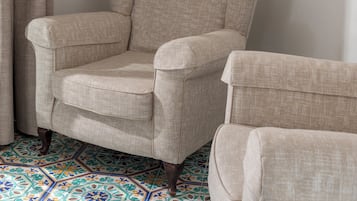 A beige armchair in a room with a patterned floor and a large mirror on the wall.