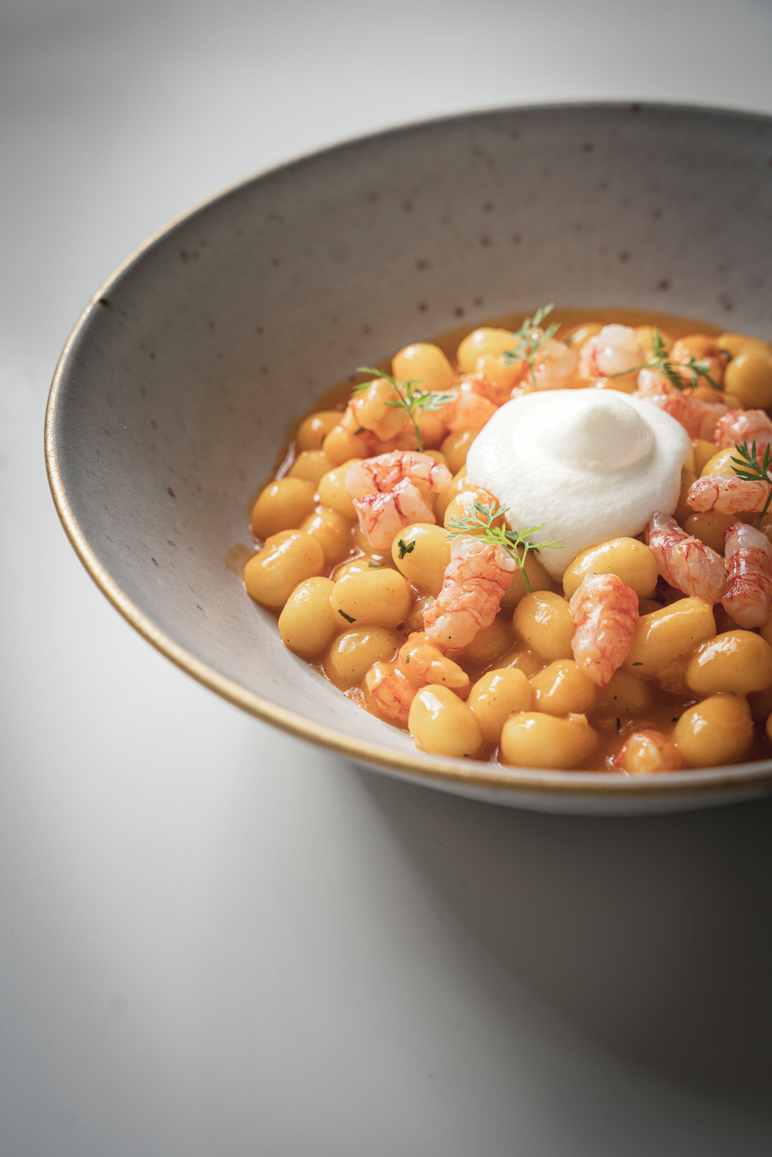 A bowl of beans with shrimp and a dollop of sour cream.